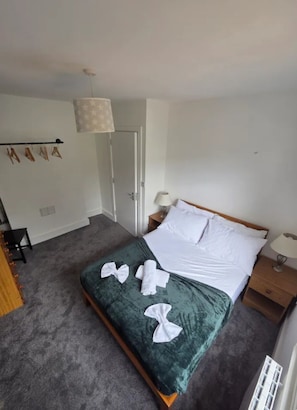 A hotel room with a bed, a nightstand, a lamp, and a hanging light fixture.