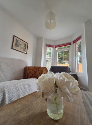 A room with a bed, a table with a vase of flowers, a framed picture on the wall, and a window with curtains. - St Mary's Cottage One
Entire 2 bedroom cottage - a home from home (Dover)