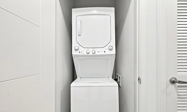 Eine weiße Waschmaschine in einem Badezimmer mit Tür und Lüftung.