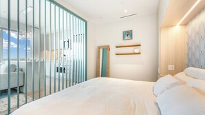 A modern bedroom with a large bed, a view of the sky through floor-to-ceiling windows, and a minimalist decor. - Luxury 1BR Residence at One GT · Rooftop Pool & Views (George Town)
