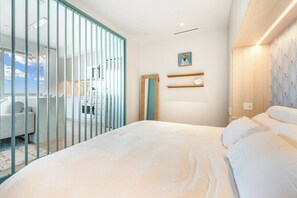 A modern bedroom with a large bed, a view of the sky through floor-to-ceiling windows, and a minimalist decor. - Luxury 1BR Residence at One GT · Rooftop Pool & Views (George Town)