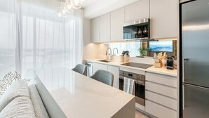 A modern kitchen with a large island, stainless steel appliances, and a view of the city. - Luxury 1BR Residence at One GT · Rooftop Pool & Views (George Town)