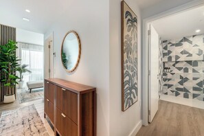 A hallway with a wooden cabinet, a mirror, and a wall with a geometric pattern. - Luxury 1BR Residence at One GT · Rooftop Pool & Views (George Town)