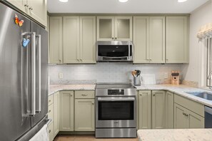 A kitchen with stainless steel appliances, light green cabinets, a microwave, an oven, and a sink. - Loggers Lookout Condo at The Homestead (Glen Arbor)