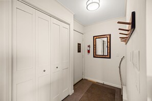 A hallway with white doors, a framed mirror, a fire extinguisher, and a wooden coat rack. - Loggers Lookout Condo at The Homestead (Glen Arbor)