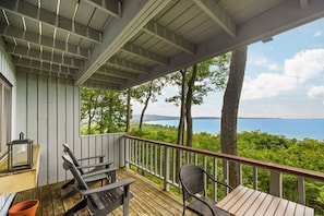 A wooden deck with outdoor furniture, a railing, and a view of a body of water. - Loggers Lookout Condo at The Homestead (Glen Arbor)