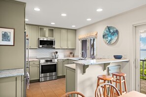 A modern kitchen with stainless steel appliances, a built-in oven, and a bar area with stools. - Loggers Lookout Condo at The Homestead (Glen Arbor)