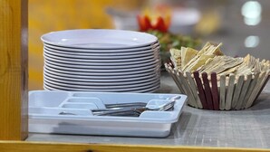 Una pila de platos blancos sobre una mesa, con una bandeja blanca que contiene cubiertos.