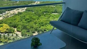 Ein Balkon mit Blick auf eine Küstenlandschaft, ein kleiner Tisch mit einer Pflanze und eine Couch mit Kissen.