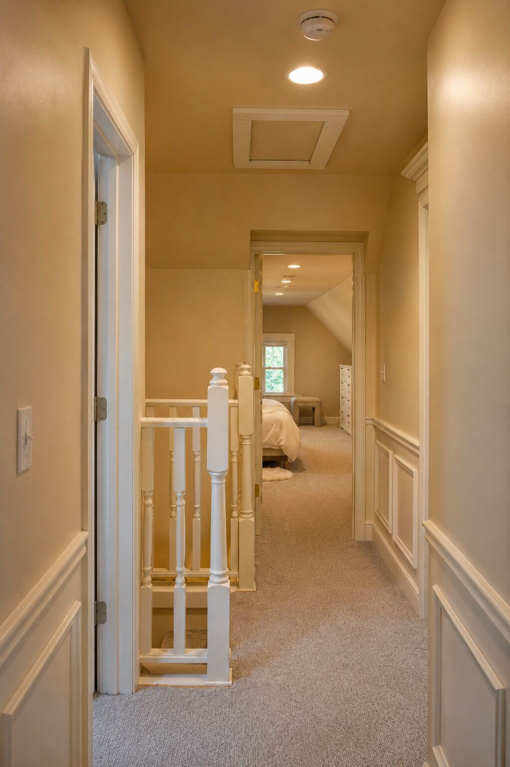 A hallway with a carpeted floor, white walls, and a door leading to a bedroom with a bed and a dresser.