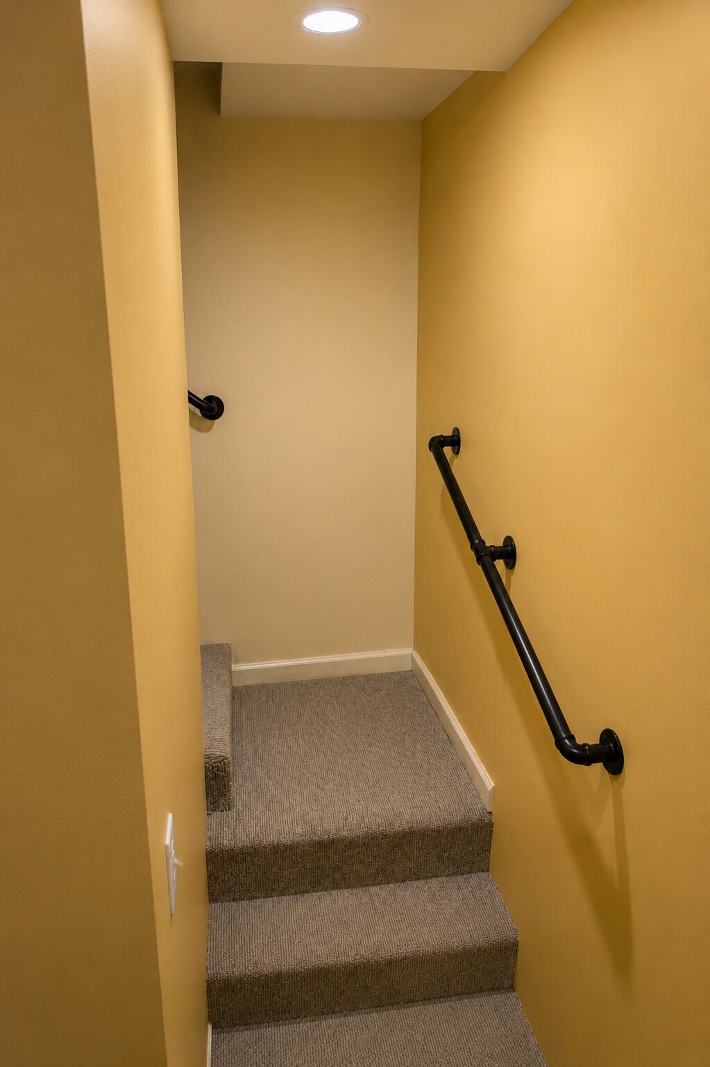 A carpeted staircase with a handrail, leading to a landing with a light fixture.
