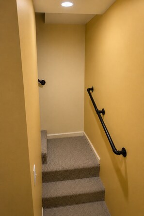 Un escalier recouvert de moquette, doté d’une rampe, menant à un palier éclairé par un luminaire.
