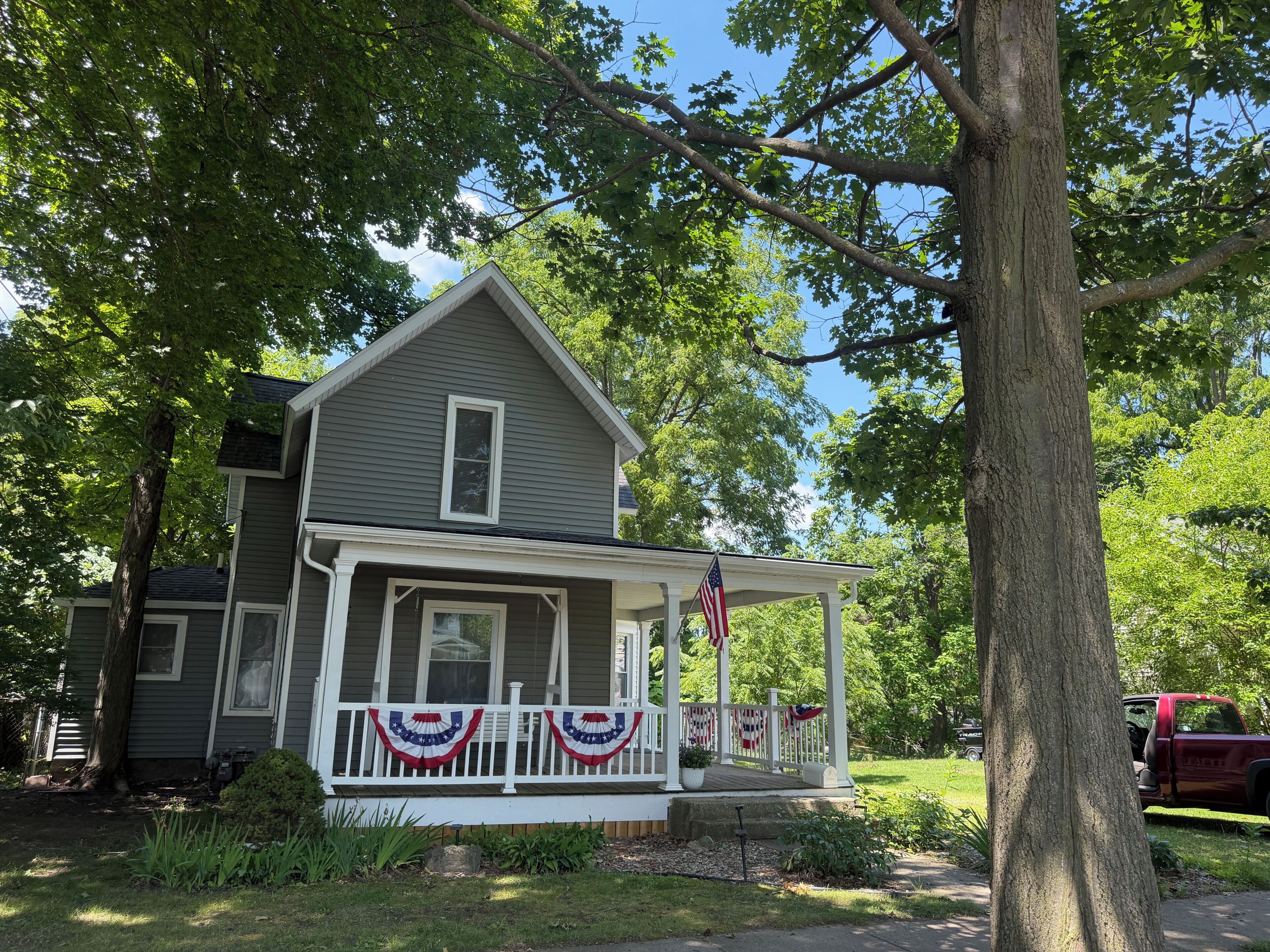 A two-story house with a porch, an American flag, and a red truck parked outside.