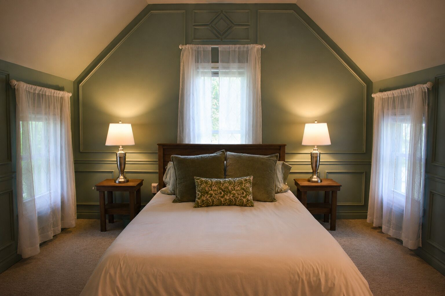 A bedroom with a large bed, two bedside tables with lamps, and a window with sheer curtains.