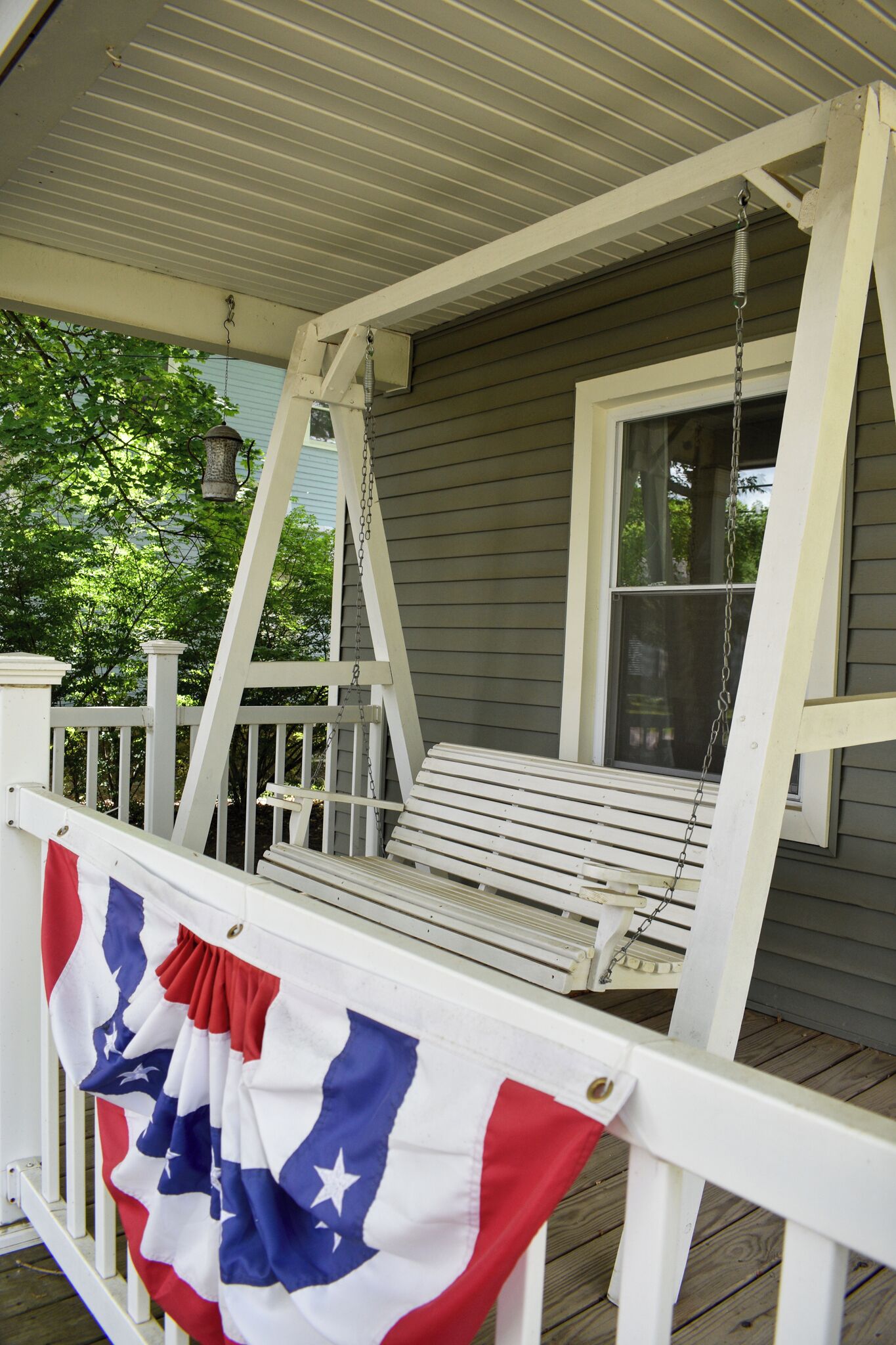 A porch with a swing chair, a flag, and a window.