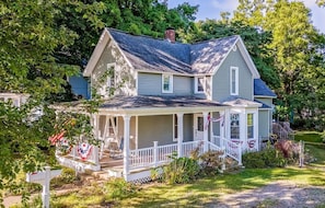 A two-story house with a porch, surrounded by greenery.