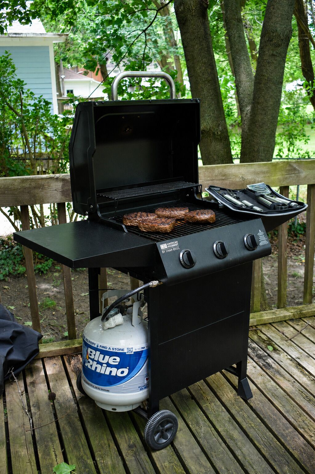 A portable grill with a propane tank on a wooden deck.