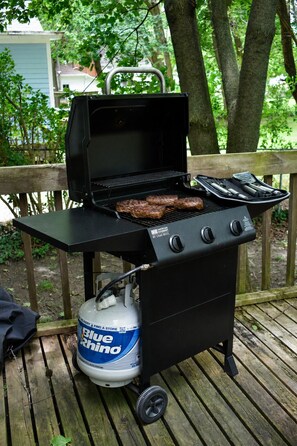 Un barbecue portatif avec une bouteille de propane, installé sur une terrasse en bois.