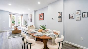 A dining area with a round table set for four, surrounded by chairs, in a room with light-colored walls and a wooden floor.