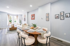 A dining area with a round table set for four, surrounded by chairs, in a room with light-colored walls and a wooden floor.