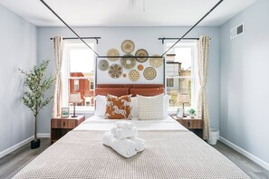 A hotel room with a bed, a wall-mounted artwork, a potted plant, and a view of the outside.