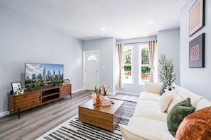 A modern living room with a flat-screen TV, a wooden entertainment unit, a white sofa, and a patterned rug.