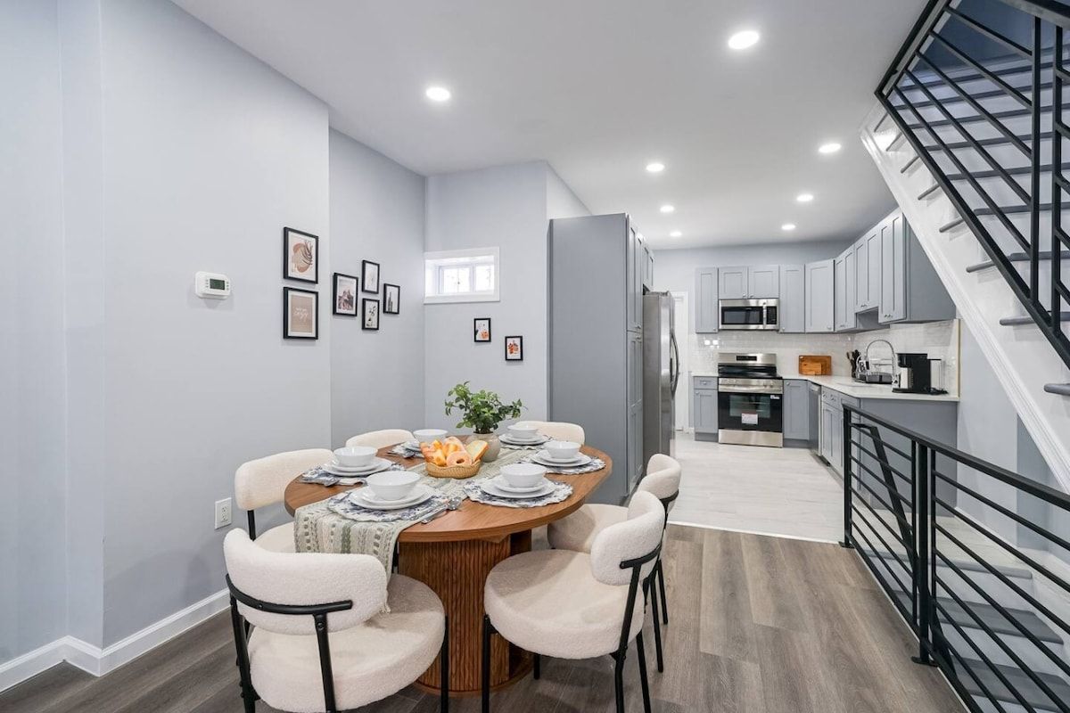 A modern dining area with a round table set for six, surrounded by light-colored chairs.