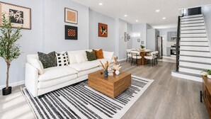 Uma sala de estar moderna com um sofá branco, uma mesa de centro e uma área de jantar com mesa e cadeiras.