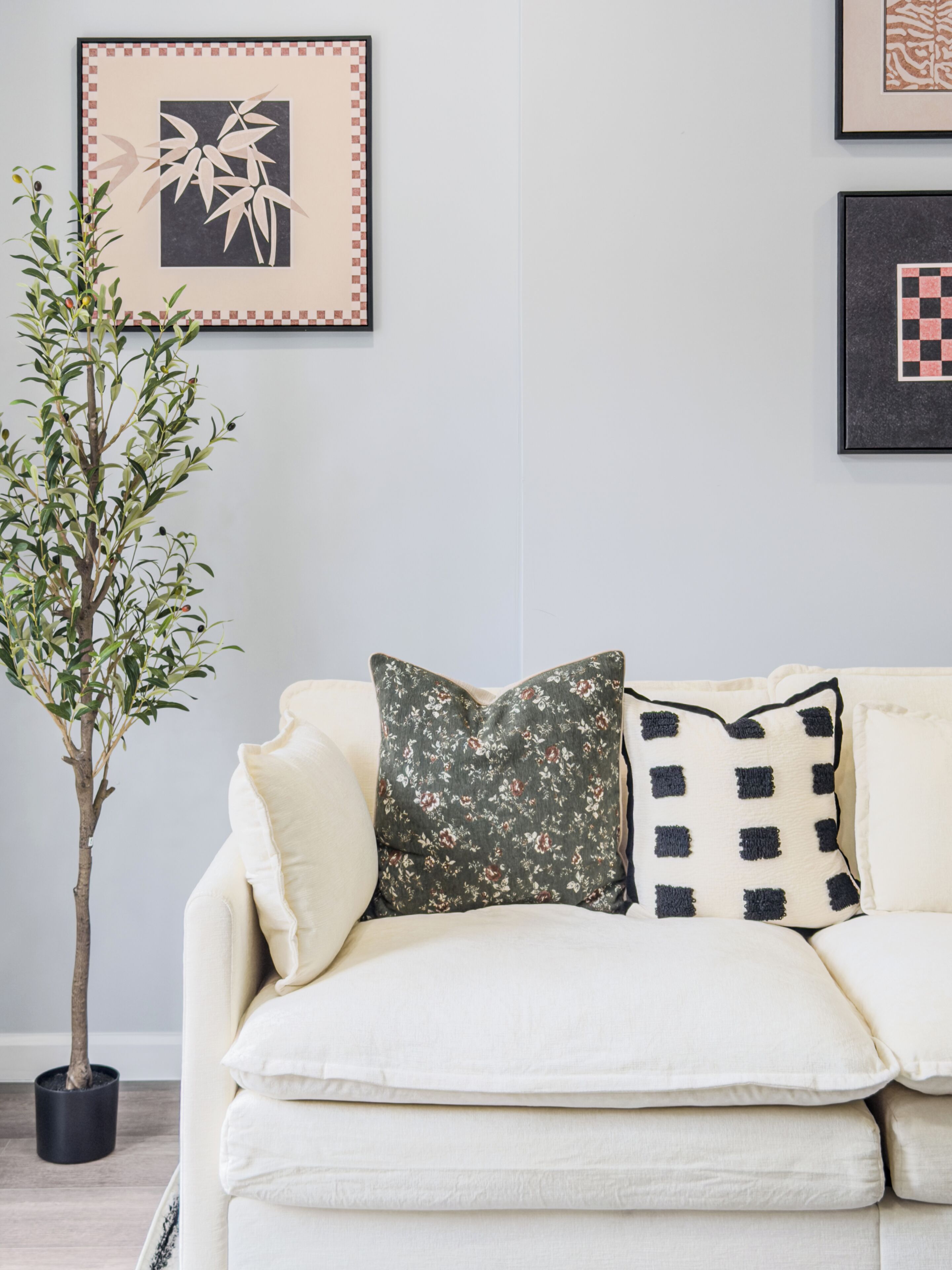Ein Zimmer mit einem weißen Sofa, einer Topfpflanze und gerahmten Bildern an der Wand.