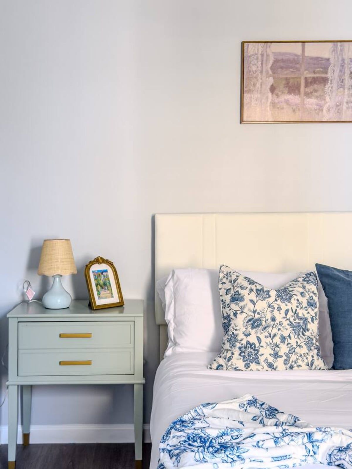 A bedroom with a bed, a nightstand, a lamp, and a framed picture.