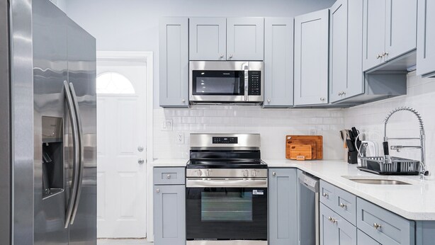 Cozinha moderna com eletrodomésticos de aço inoxidável, armários cinza e painel de azulejos branco.