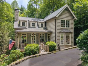 A two-story house with a stone chimney, a porch with a railing, and an American flag. - Cashiers 3-bedroom home in Trillium (Cashiers)