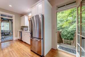 A modern kitchen with stainless steel appliances, wooden flooring, and a view of a lush garden through a glass door. - Cashiers 3-bedroom home in Trillium (Cashiers)