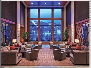 Eine großzügige Lobby mit einem großen Fenster und Bergblick, mehreren Sitzbereichen und dekorativer Beleuchtung.