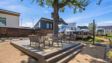 Un patio con mobiliario exterior, un árbol y un edificio al fondo.