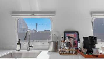 Una cocina con un lavamanos de acero inoxidable, una cafetera y un ventanal con vistas a edificios.