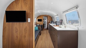 A compact interior with a wooden accent wall, a kitchenette, and a seating area. - Private Airstream on a Hidden Courtyard Near Downtown (Fort Worth)
