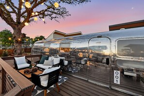 Une remorque immobile dotée d’une terrasse aménagée avec des meubles d’extérieur et un arbre.