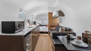 A compact, modern kitchenette with a microwave, coffee maker, and a small dining area with a table and chairs. - Private Airstream on a Hidden Courtyard Near Downtown (Fort Worth)