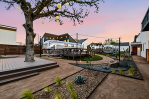 Un espacio exterior moderno con un árbol, una terraza de madera y una estructura de vidrio.