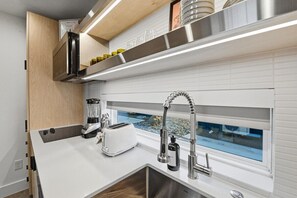 Une cuisine compacte équipée d’un grille-pain encastré, d’un mixeur, d’une hotte aspirante en acier inoxydable et d’une fenêtre donnant sur un paysage rocheux.
