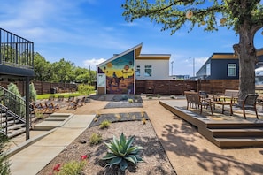 Un patio exterior moderno con un mural, arreglos de asientos y un jardín ajardinado.