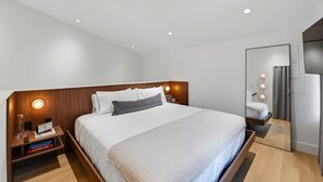 Una camera d'albergo moderna con un letto grande, comodini, uno specchio e luci a incasso nel soffitto.