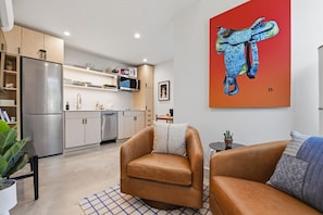 A modern kitchen with stainless steel appliances, a dining area with leather chairs, and a large abstract painting on the wall. - King casita with parking, minutes to downtown (Fort Worth)