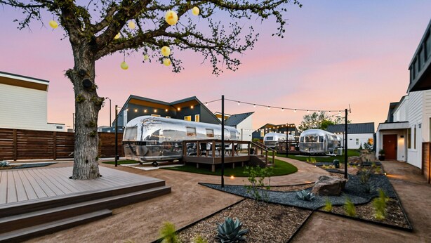 Ein moderner Außenbereich mit Baum, Holzterrasse und Glasbau.