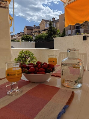 A table with a bowl of strawberries, a glass of coffee, and a water bottle.
