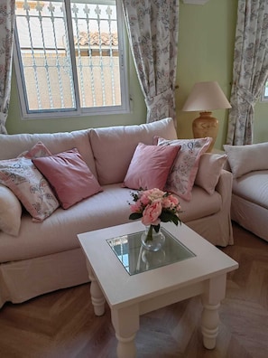 A living room with a sofa, a glass coffee table, and a vase with flowers.
