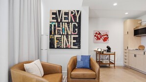 A modern living room with a sofa and armchair, a kitchen area with wooden cabinets, and a large abstract painting on the wall. - Hideaway Designer Casita, Minutes to Downtown & TCU (Fort Worth)