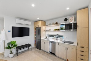 A modern kitchen with a flat-screen TV, stainless steel appliances, and a bench. - Hideaway Designer Casita, Minutes to Downtown & TCU (Fort Worth)
