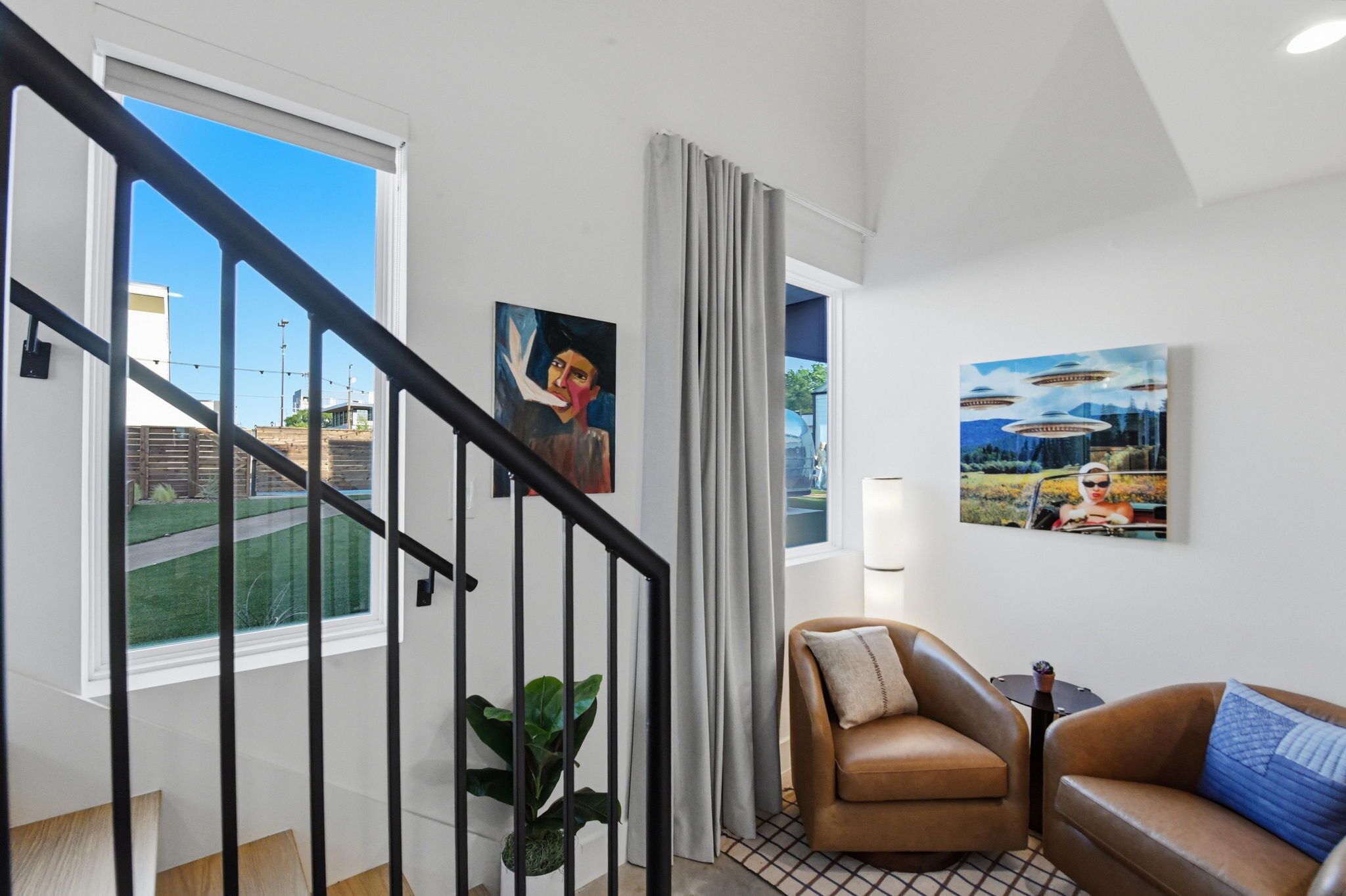 A modern living room with a staircase, a sofa, a chair, and two paintings on the wall.